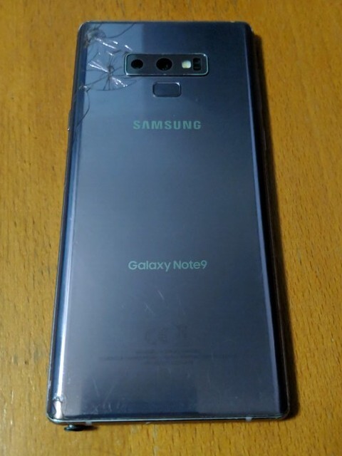 The back of my Samsung Galaxy Note 9, in Lavender Purple. The top-left corner of the back glass is cracked. There is a replacement S-Pen sticking out from the bottom-left of the phone.